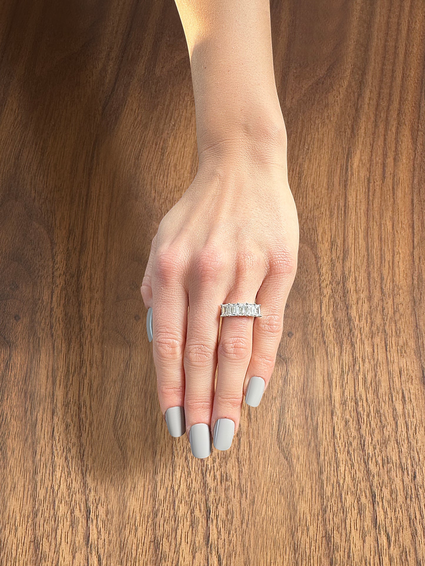 A hand with a silver diamond ring rests on a wooden surface.