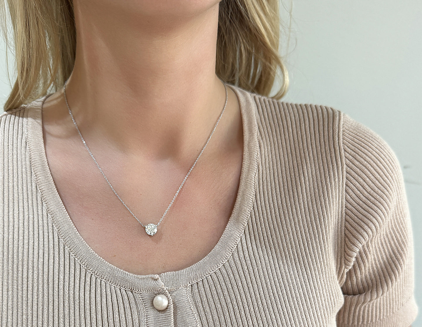 Delicate silver necklace with a heart-shaped pendant, worn with a ribbed beige top.