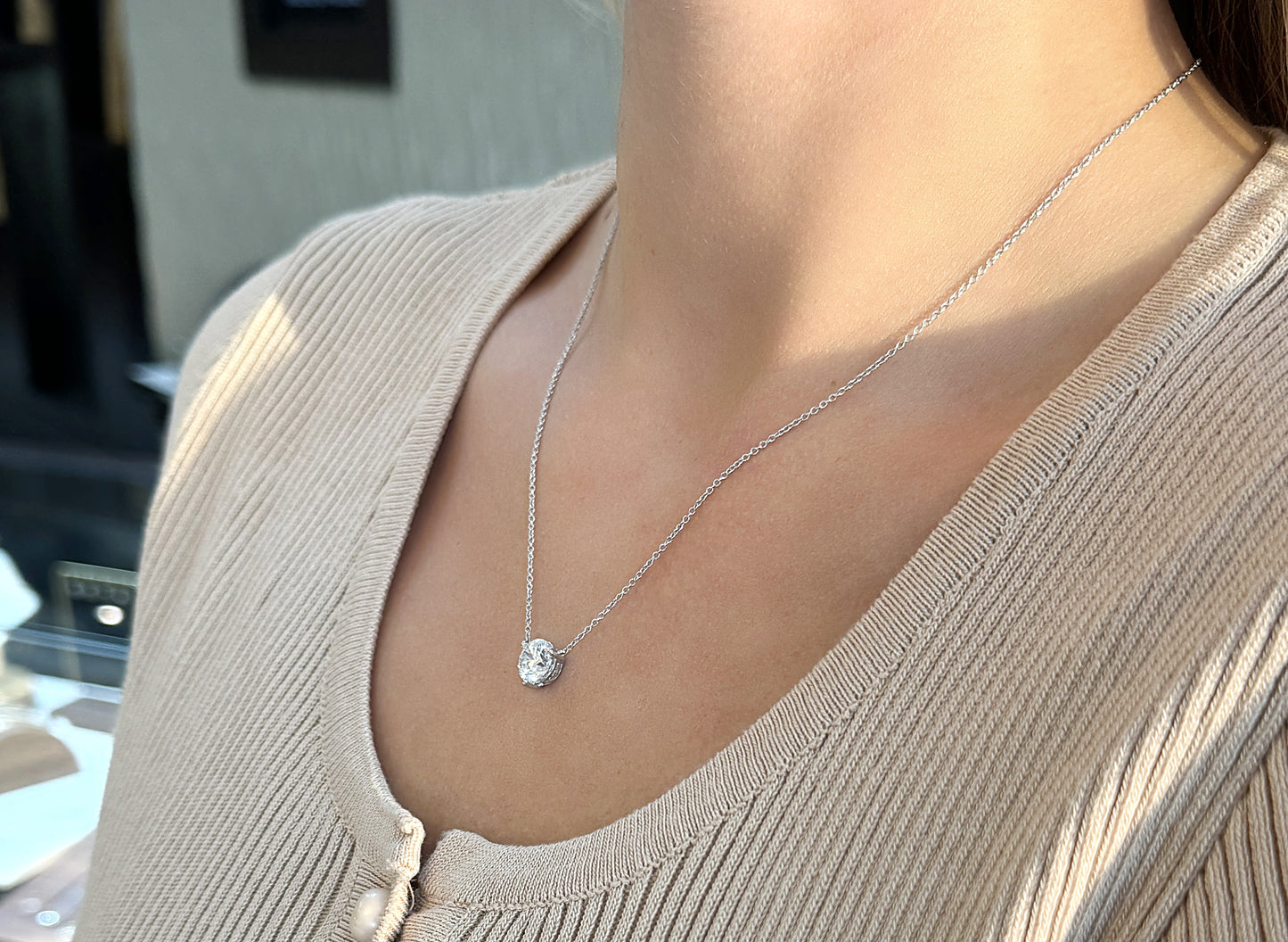 Delicate silver necklace featuring a sparkling pendant, worn on a beige top.
