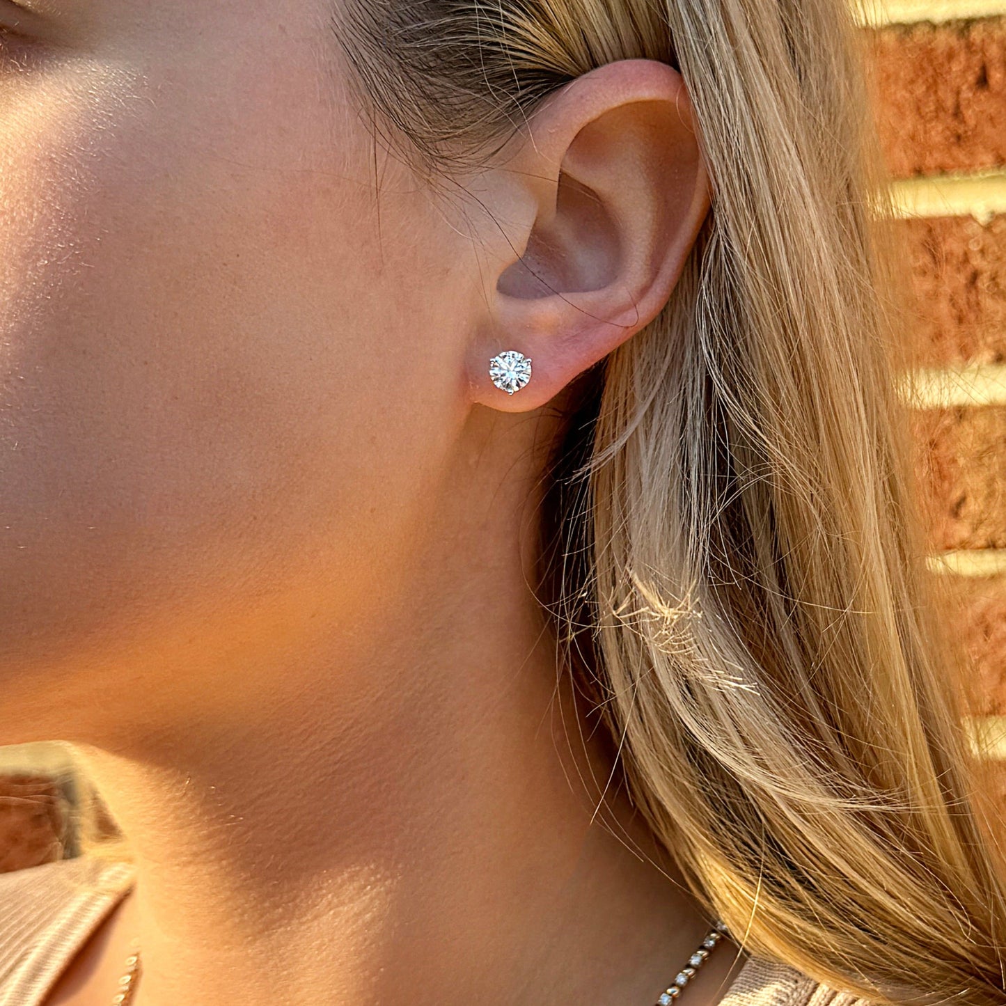 Close-up of a woman wearing a sparkling diamond stud earring against a brick background.