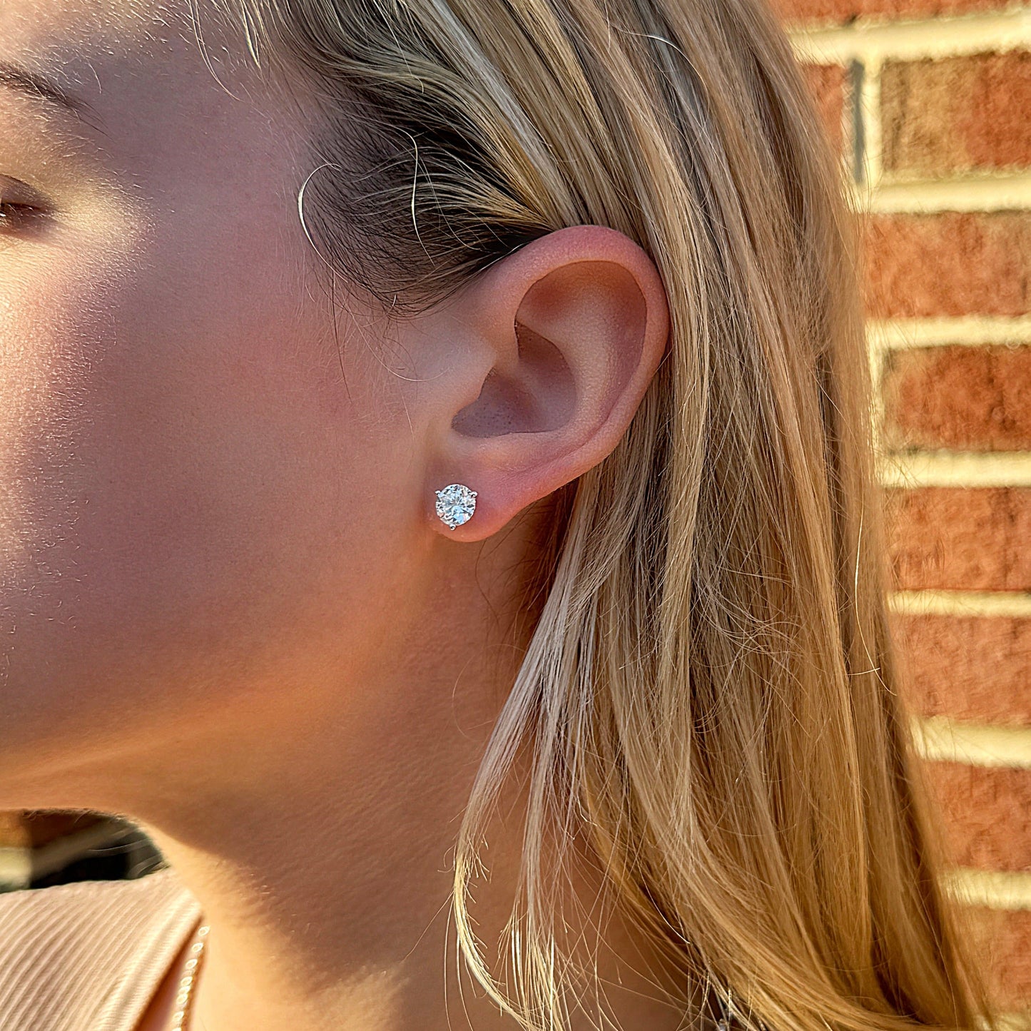 Close-up of a woman wearing sparkling stud earrings, with textured hair and a brick background.
