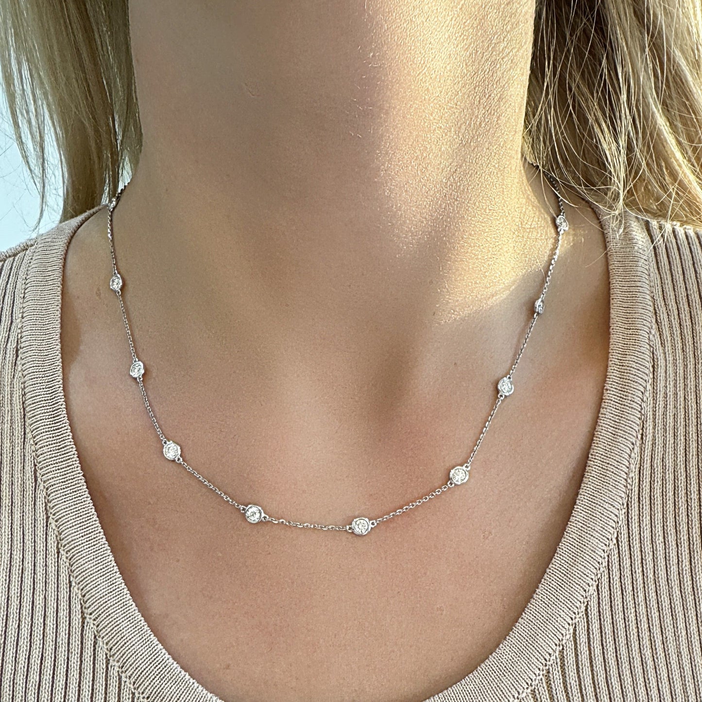 Delicate silver necklace with spaced diamond accents, worn on a light-colored top.