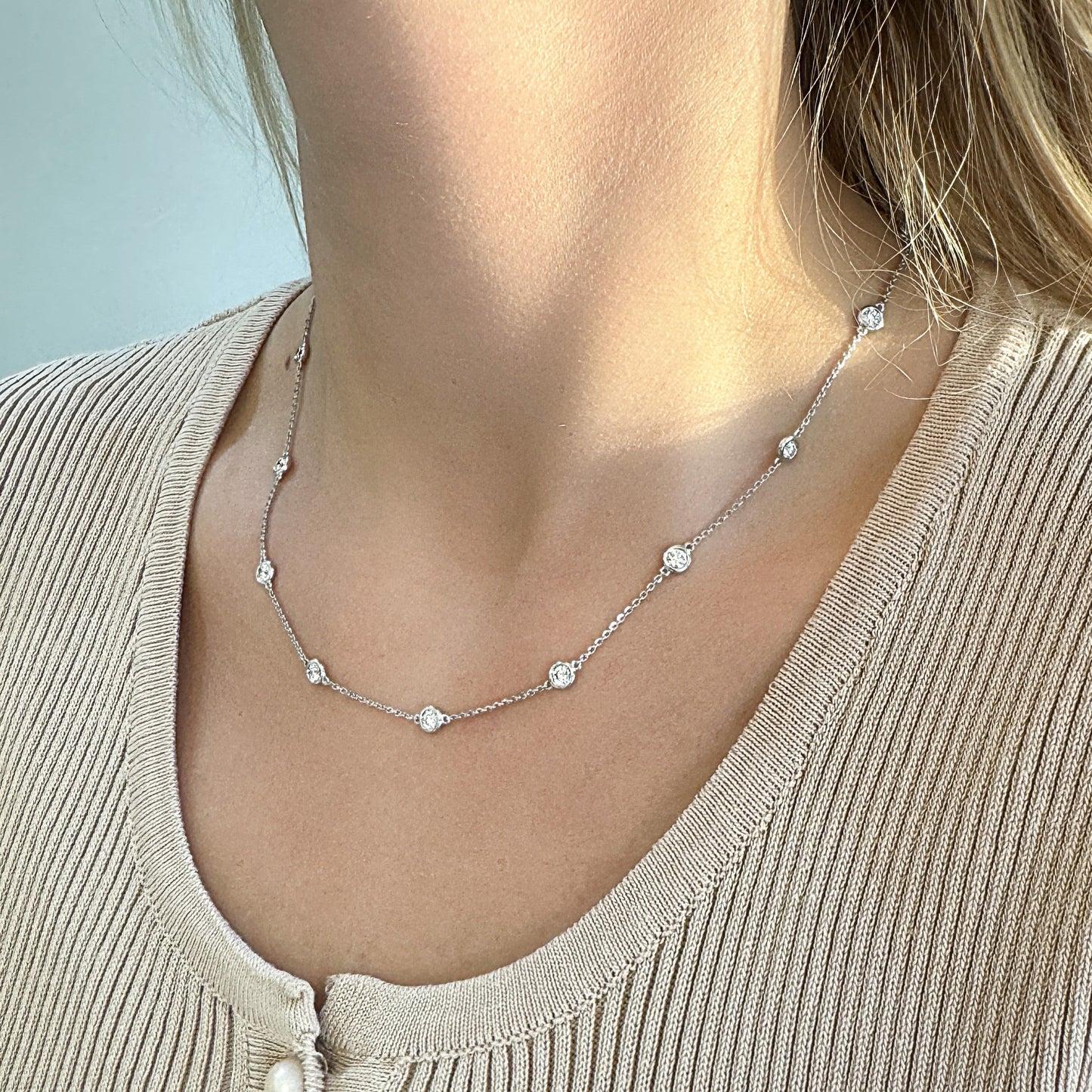Delicate silver necklace with sparkling circular pendants, worn by a person.