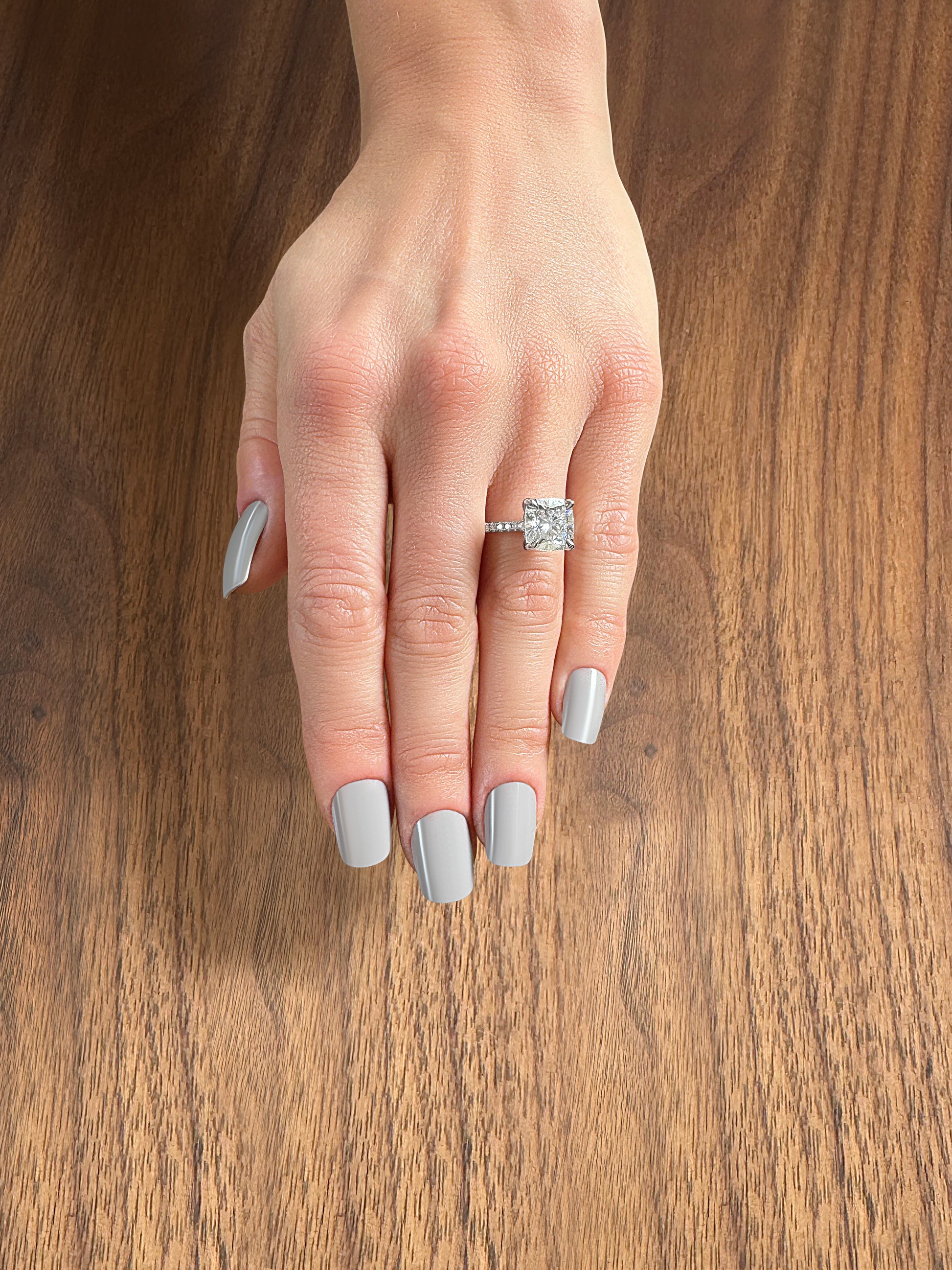A hand with long, gray manicured nails showcasing a square diamond engagement ring on the ring finger.