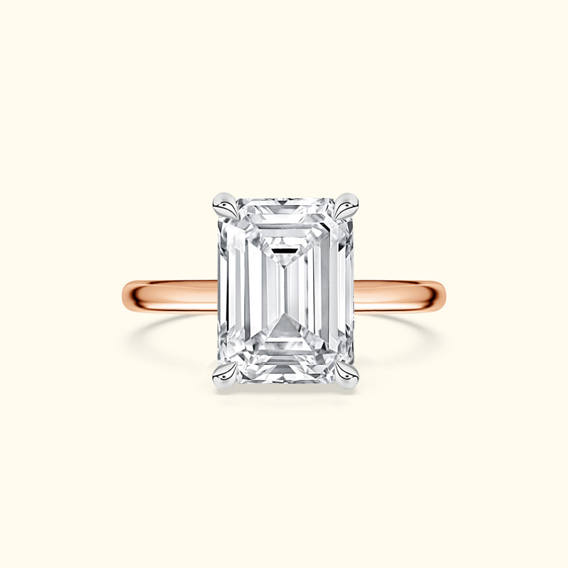 Emerald-cut diamond ring with a rose gold band on a light background.
