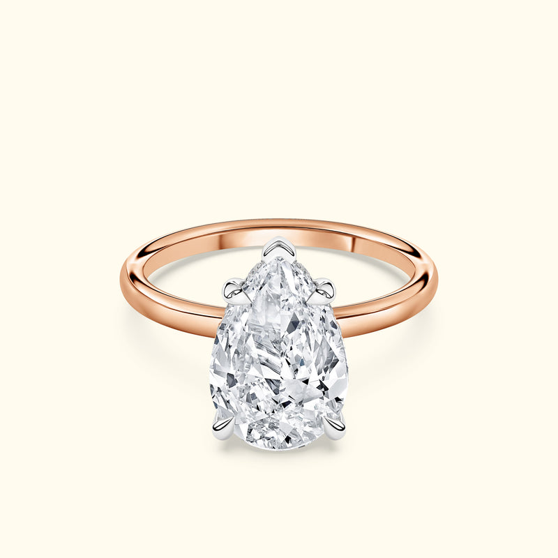Pear-shaped diamond ring with a rose gold band on a light background.