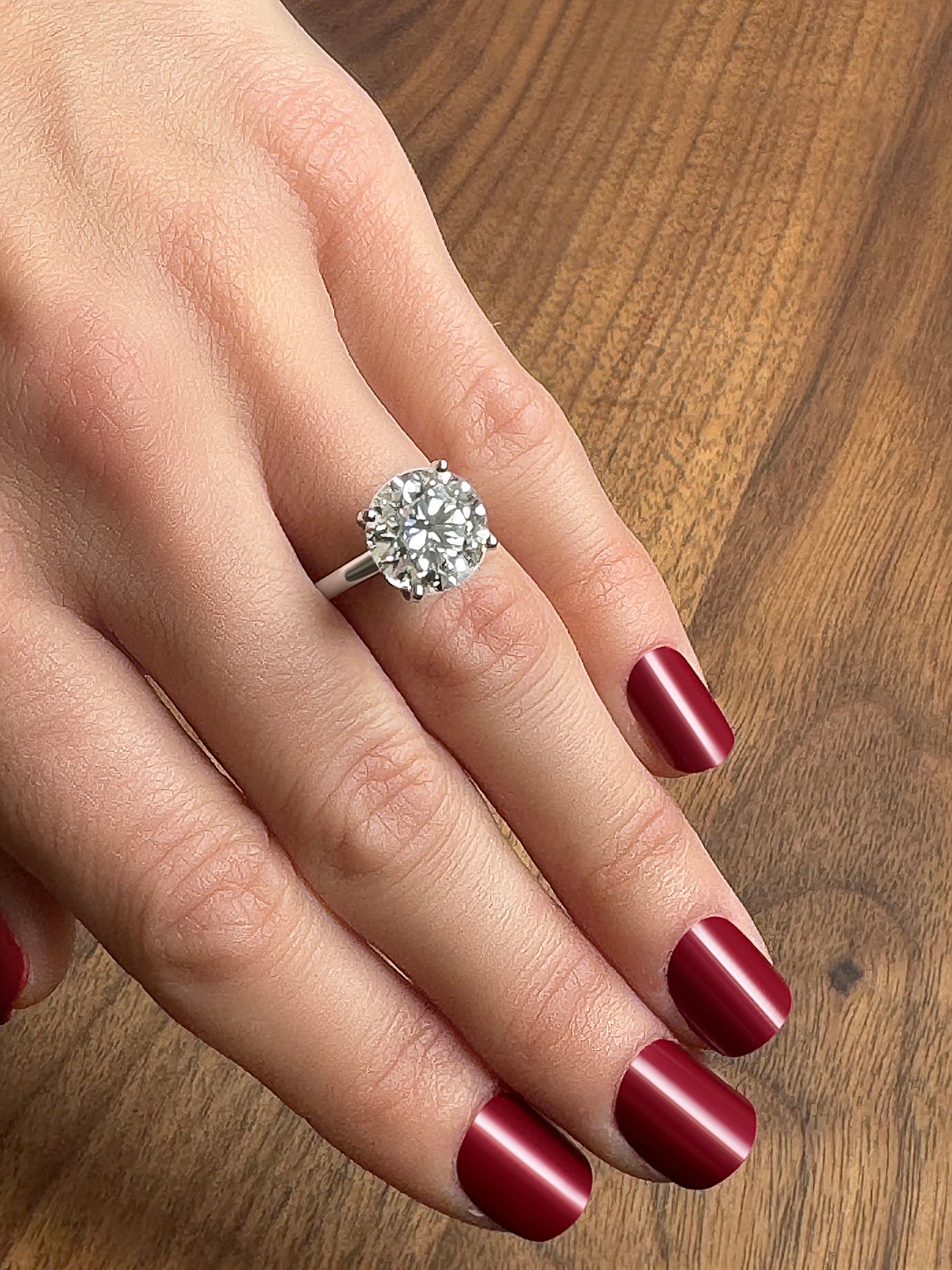 A hand with a sparkling diamond engagement ring on a manicured hand with deep red nails.
