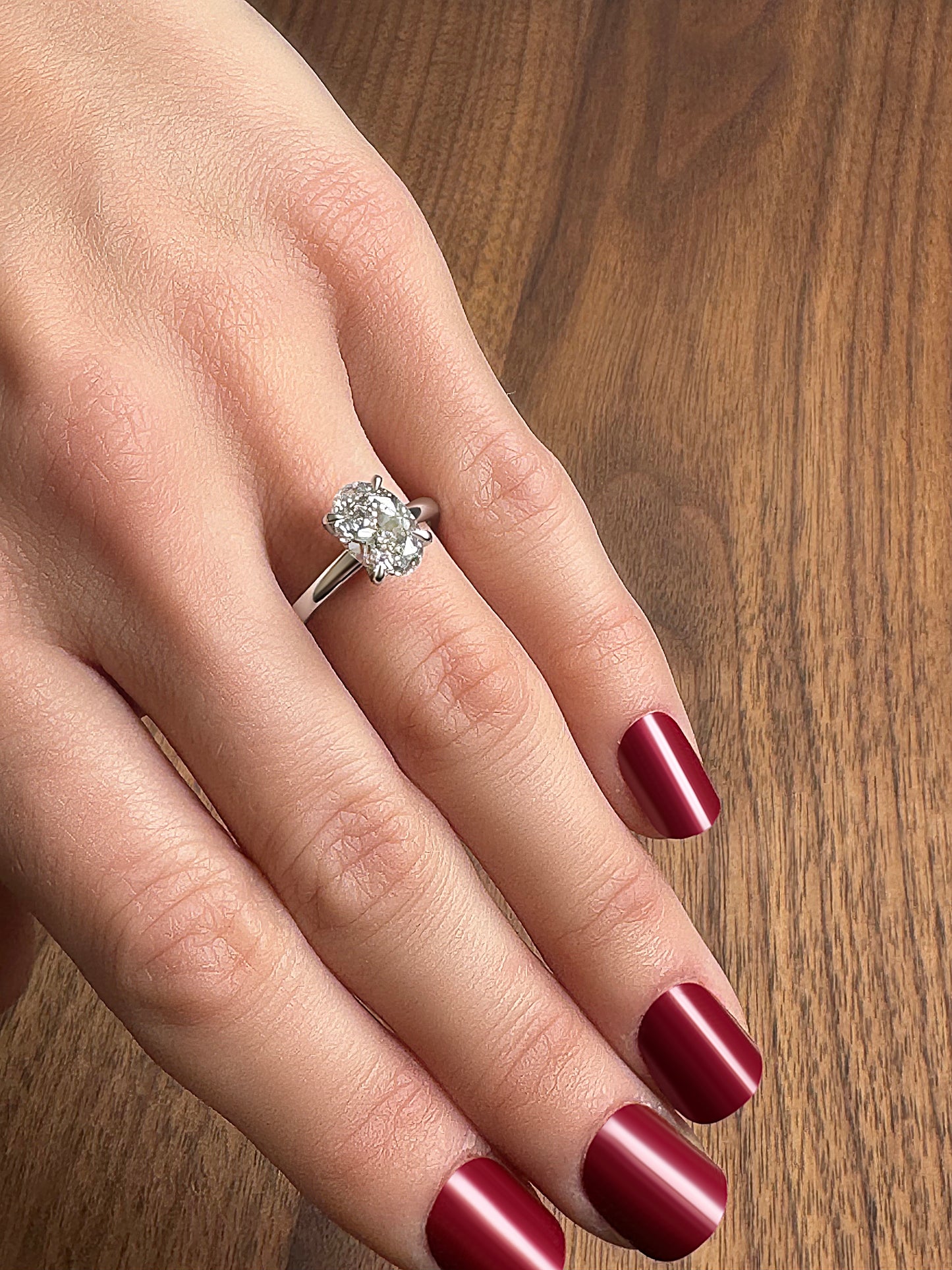 Elegant silver ring with a large central diamond on a hand with deep red nail polish.