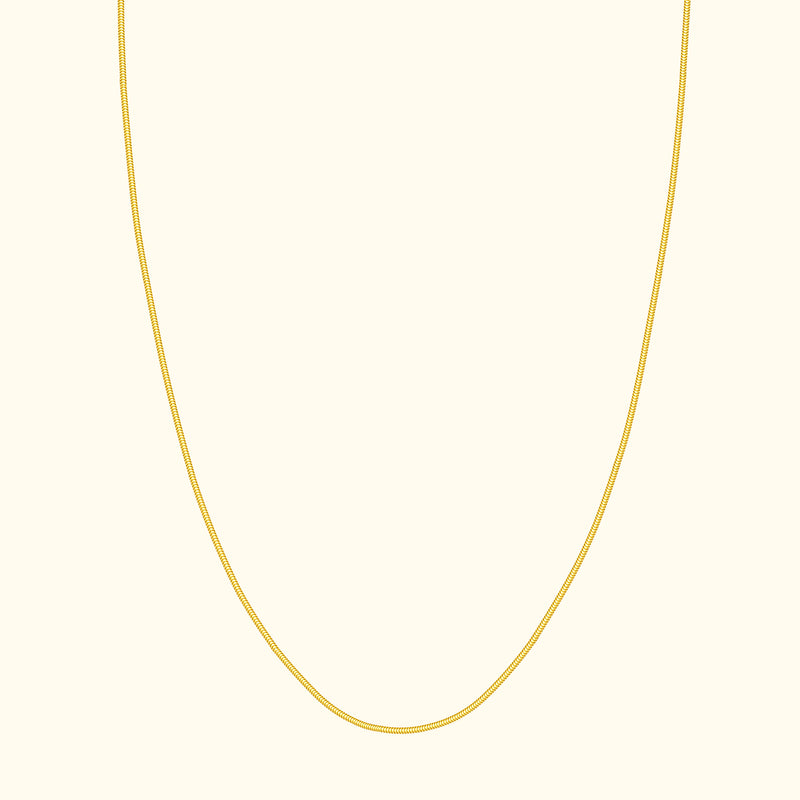 Thin gold necklace elegantly draped against a cream background.
