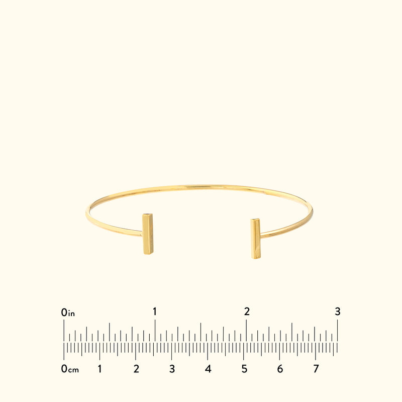 Simple gold cuff bracelet with two vertical ends, set against a light background.