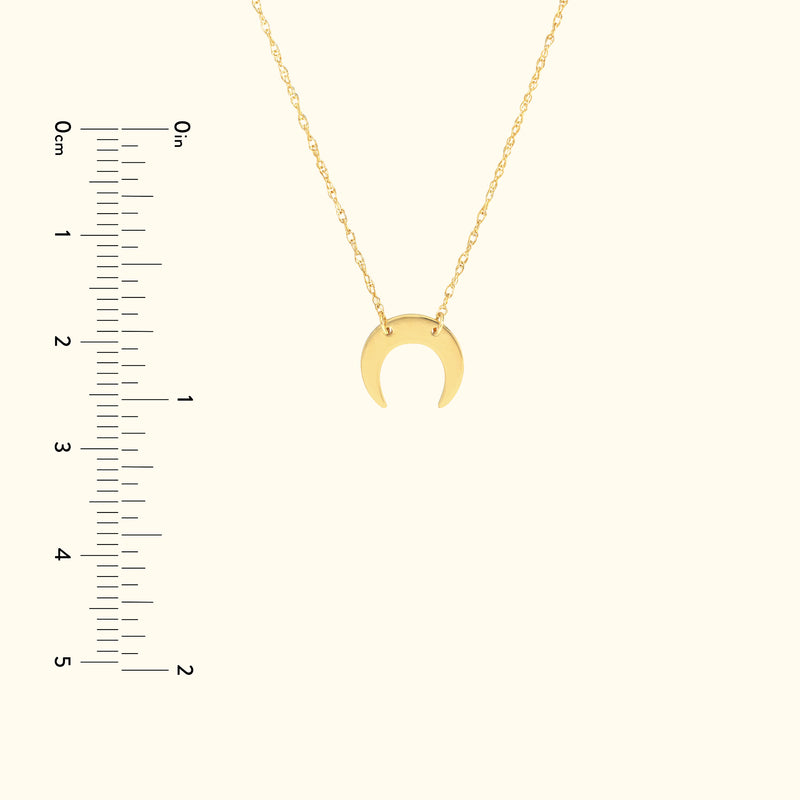 Gold crescent moon pendant on a delicate chain with a ruler for size reference.