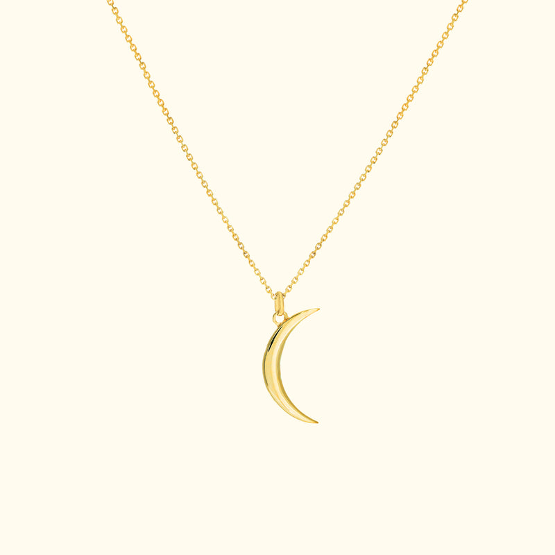 Gold crescent moon pendant on a delicate chain necklace against a light background.