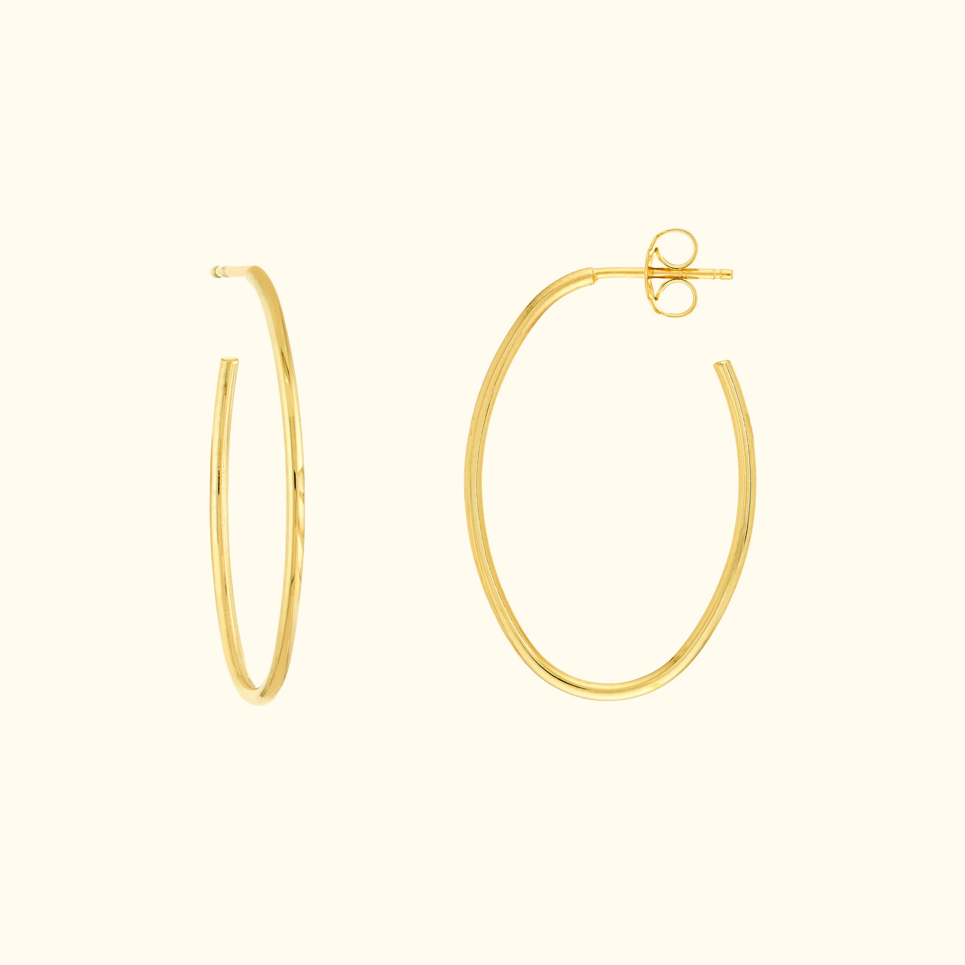 Simple gold hoop earrings, one slightly open, on a light beige background.