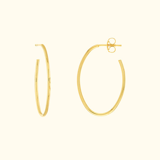 Simple gold hoop earrings, one slightly open, on a light beige background.