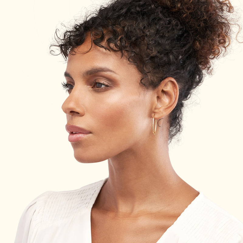 A woman with curly hair wears elegant gold hoop earrings, looking thoughtfully to the side.