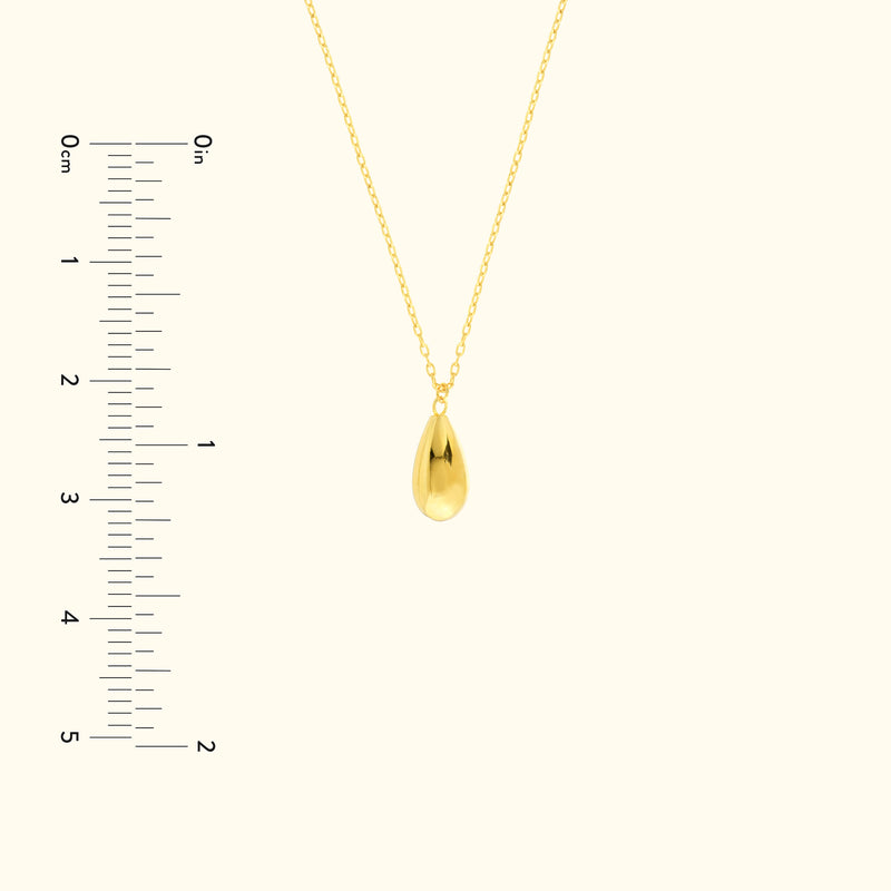 Gold teardrop pendant necklace on a delicate chain, with a measuring scale beside it.
