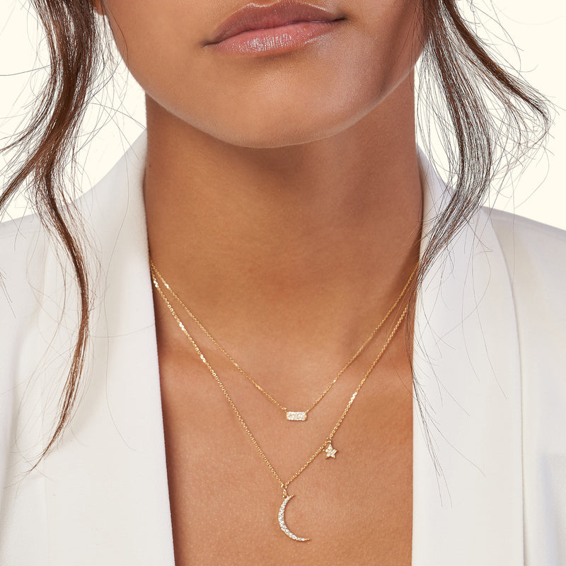 Three delicate gold necklaces layered together, featuring a crescent moon, a star, and a bar pendant.