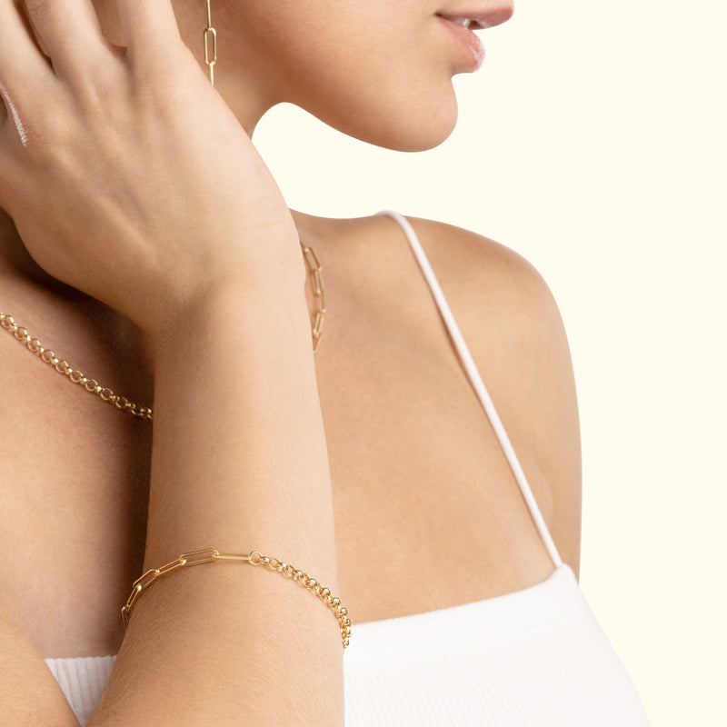Close-up of a woman wearing a gold chain bracelet and a delicate necklace, with soft lighting.