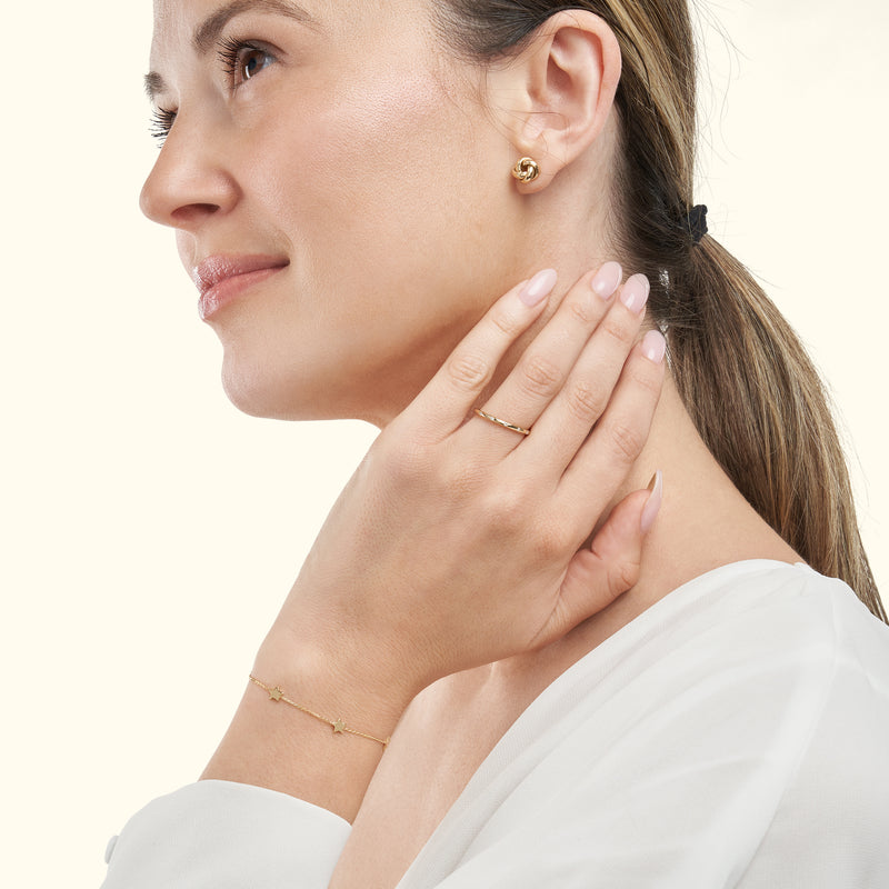 Woman wearing a gold ring and bracelet, with stud earrings, smiling softly.