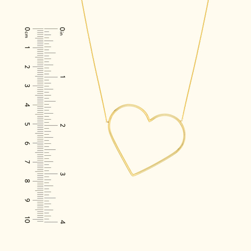 Gold heart-shaped necklace with a delicate chain, shown next to a ruler for scale.