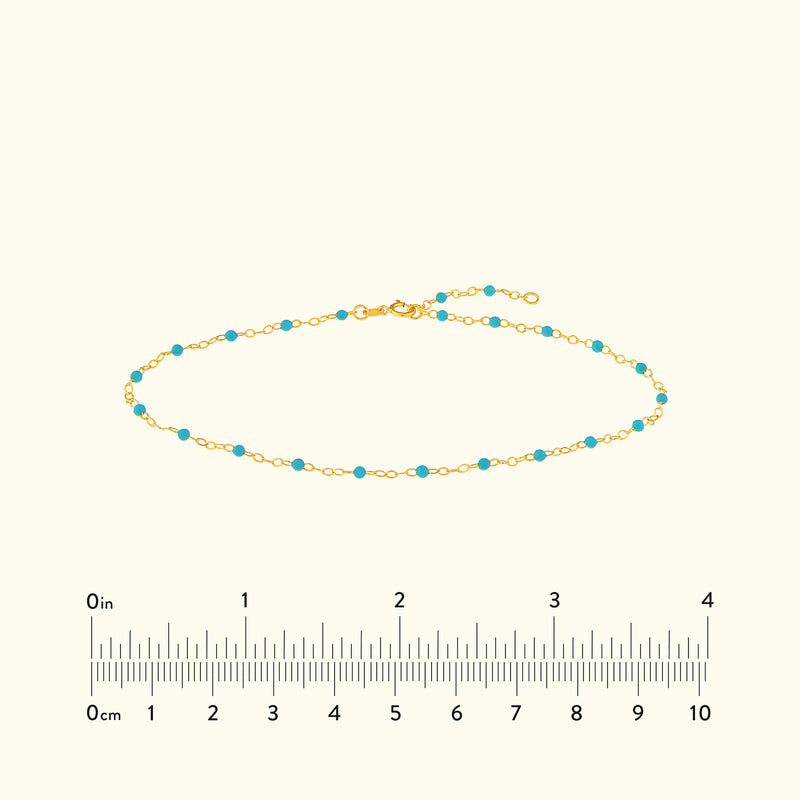Delicate gold bracelet with small turquoise beads, laid over a light background.