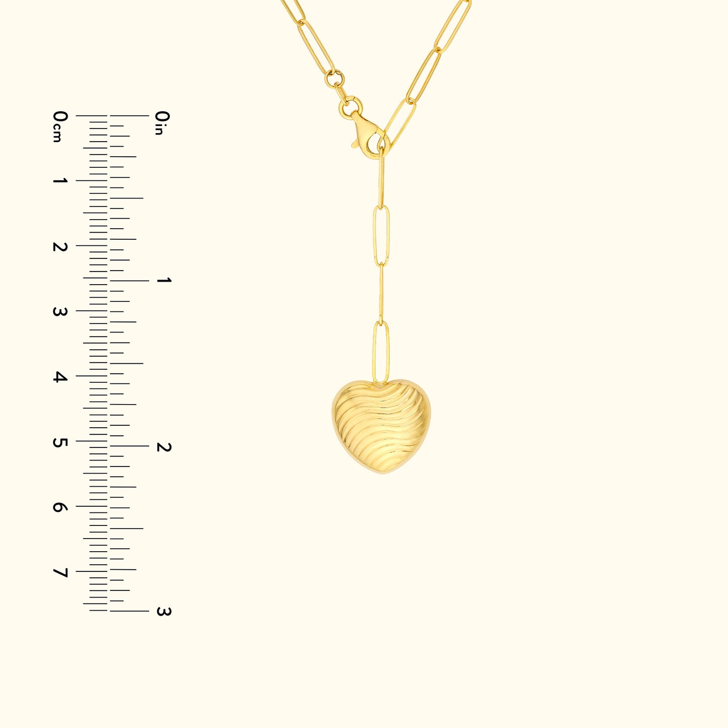 Gold heart pendant hanging from a delicate chain, next to a ruler for size reference.