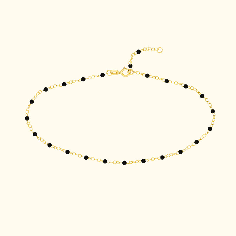 Delicate gold bracelet with black beads, featuring a clasp and adjustable chain.