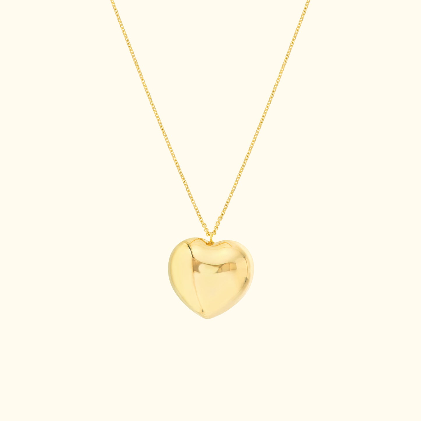 Shiny gold heart pendant on a delicate chain against a light background.