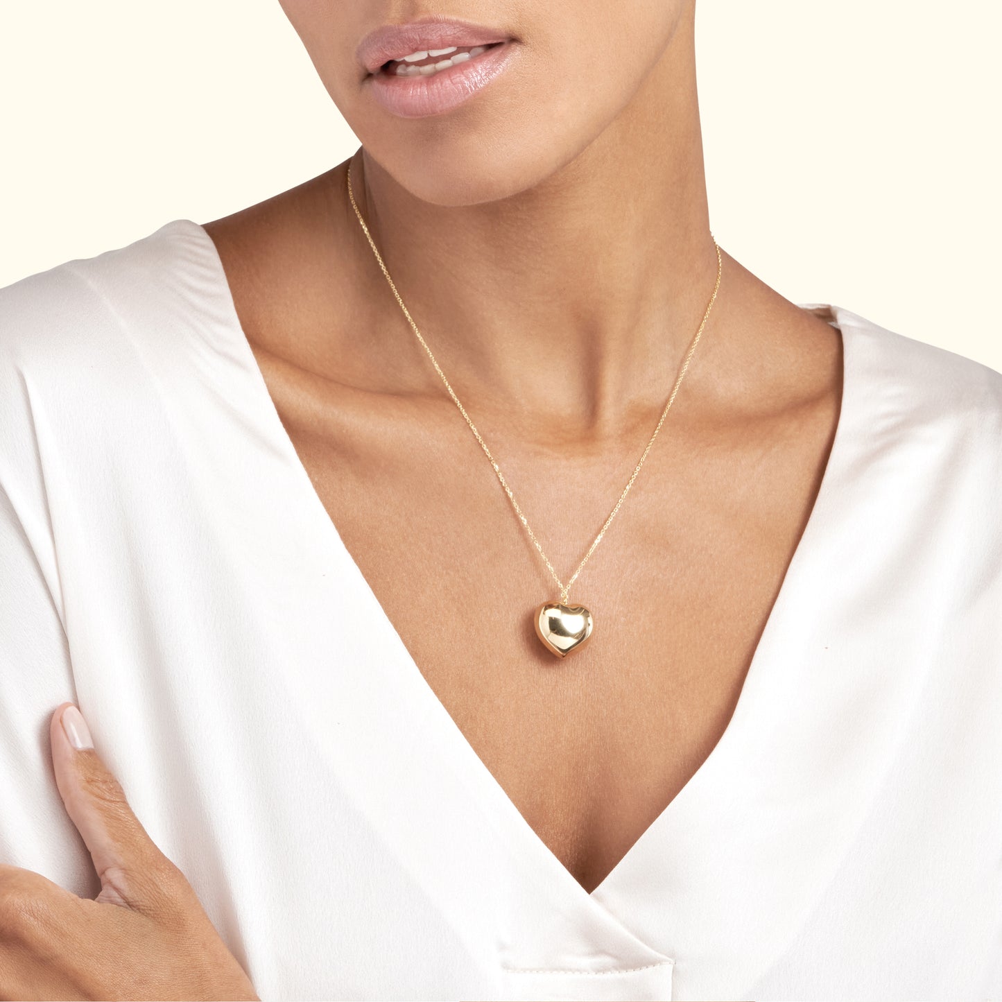 Gold heart pendant necklace worn by a woman in a silky white blouse.