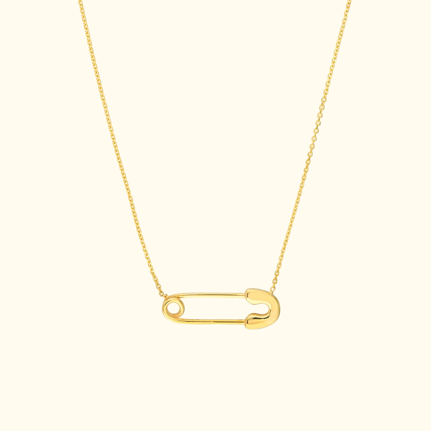Gold necklace featuring a minimalist safety pin pendant on a delicate chain.