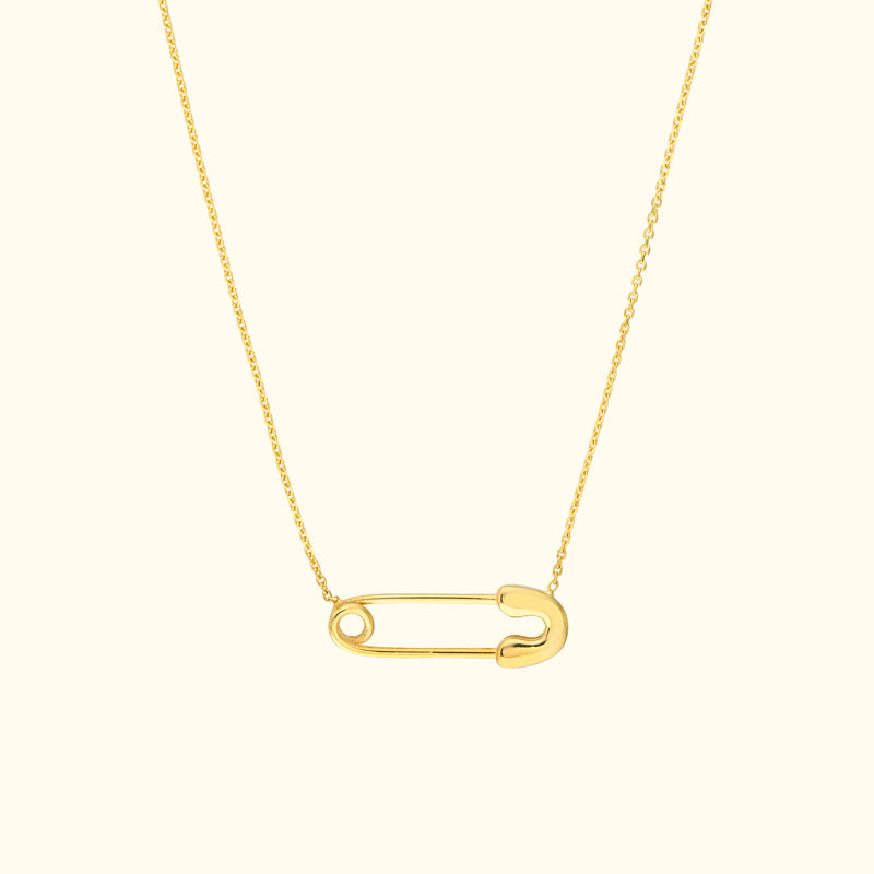 Gold necklace featuring a minimalist safety pin pendant on a delicate chain.