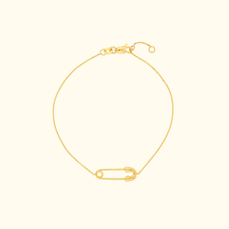 Gold chain bracelet featuring a decorative safety pin charm.