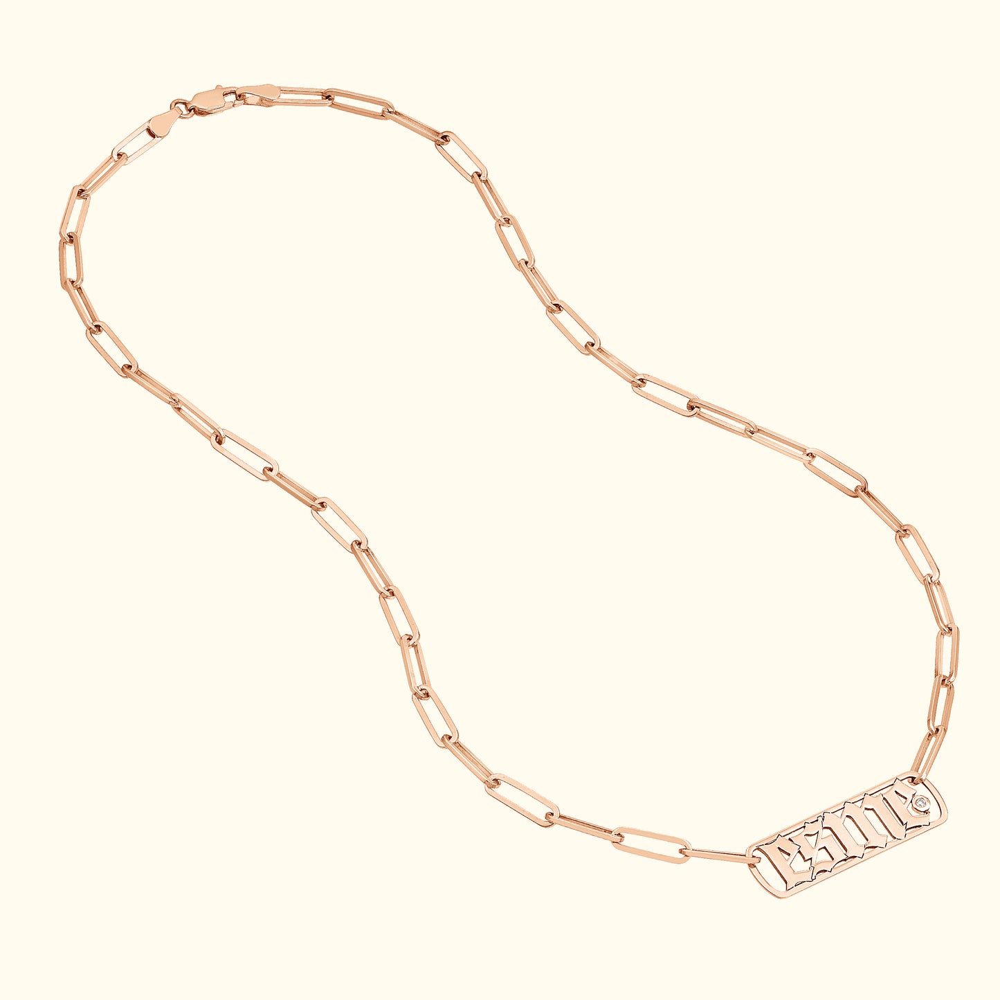 Rose gold chain necklace with a rectangular pendant featuring embossed letters.