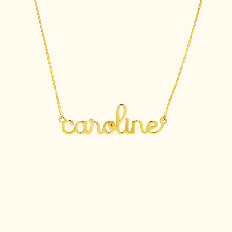 Gold name necklace featuring the word "caroline" in a cursive font.