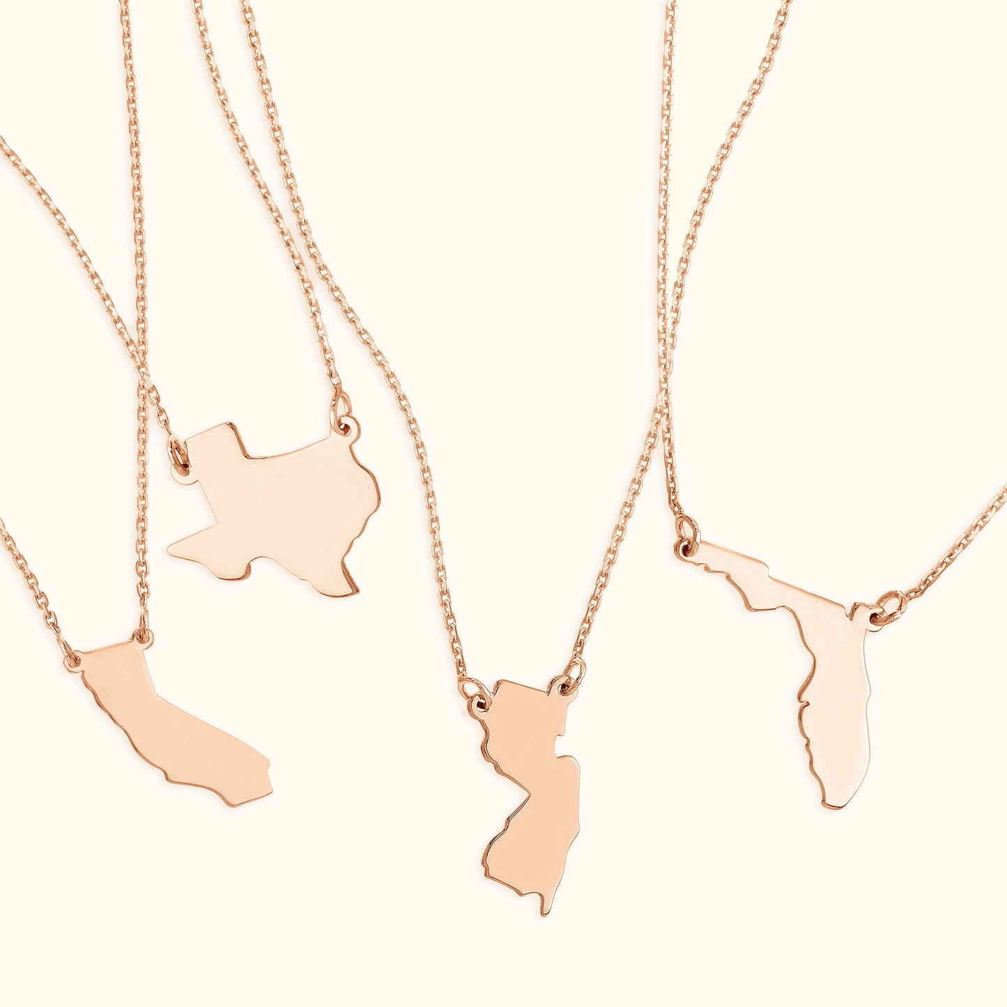 Four rose gold necklaces featuring distinct state-shaped pendants.