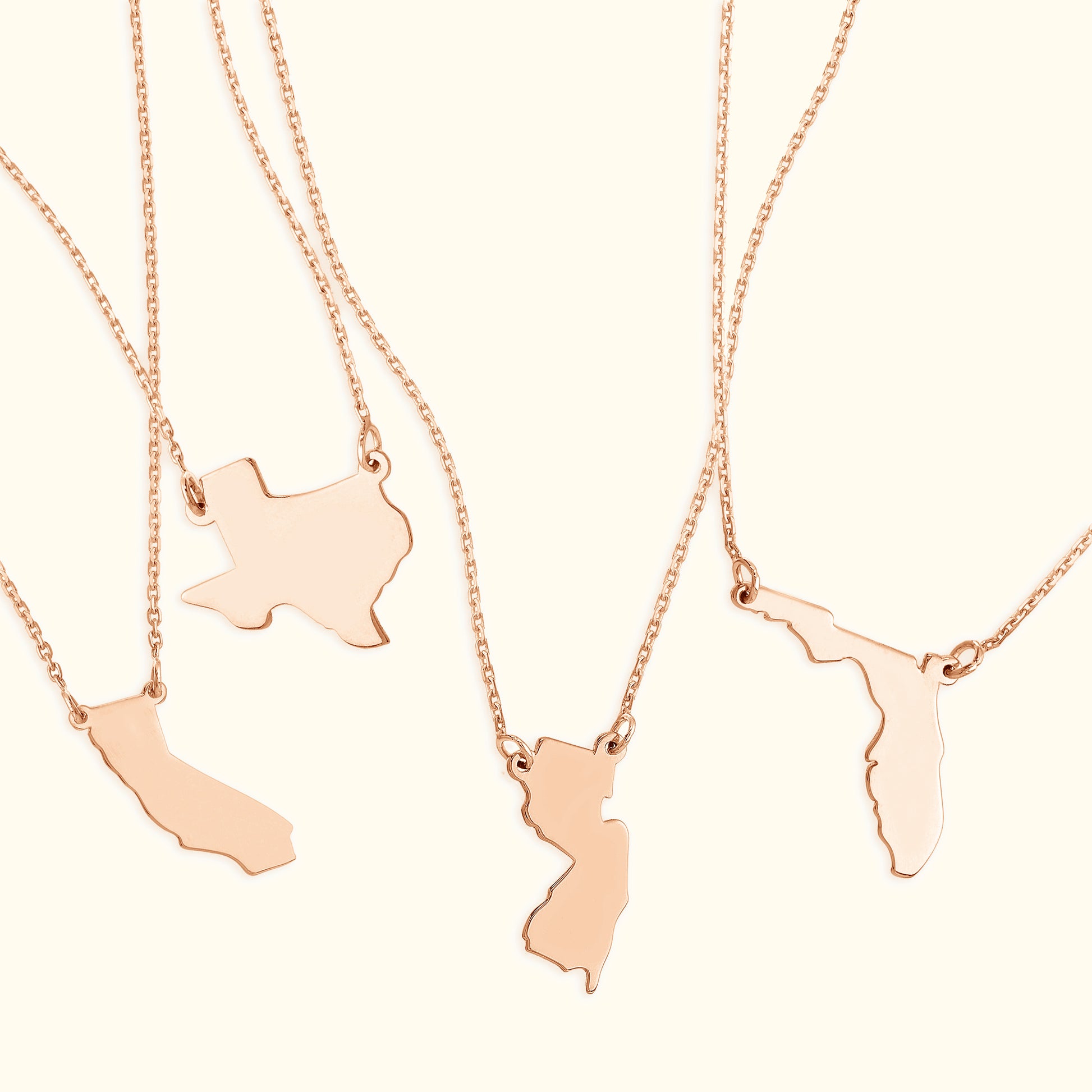 Four rose gold necklaces featuring distinct state-shaped pendants.