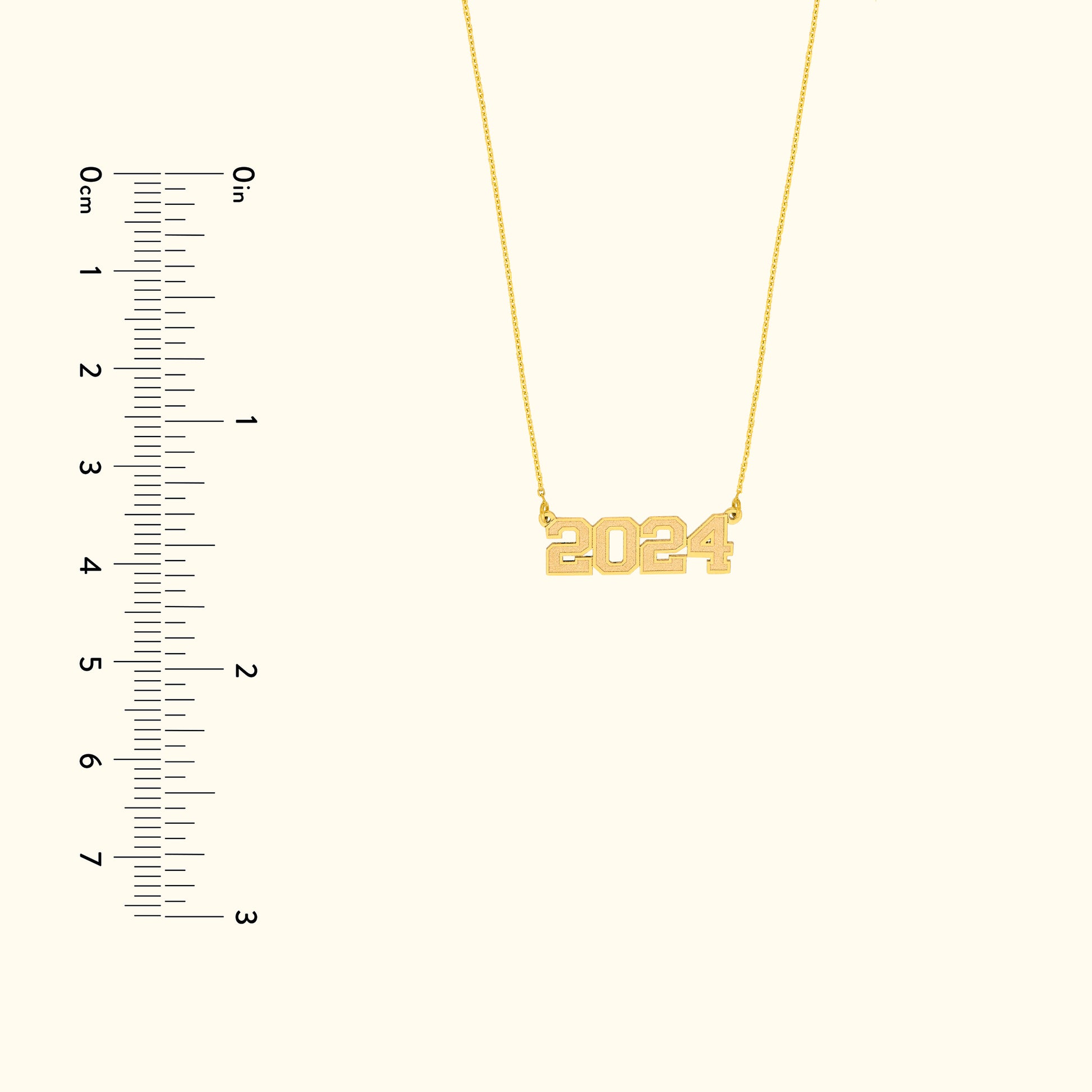 Gold necklace featuring the year "2024" as a pendant, displayed alongside a measuring ruler.