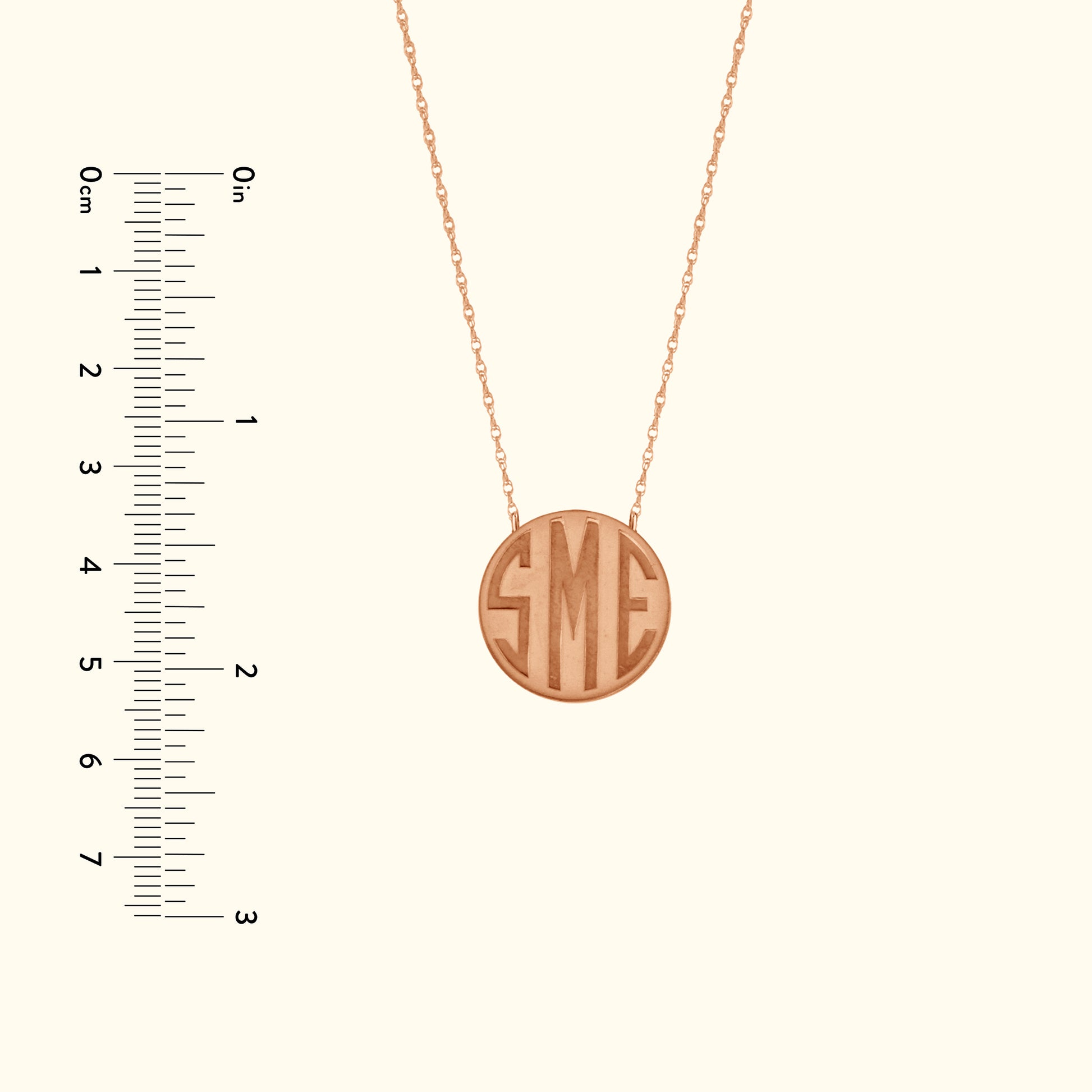 Rose gold necklace with circular pendant featuring engraved initials "SME". Ruler for size reference.