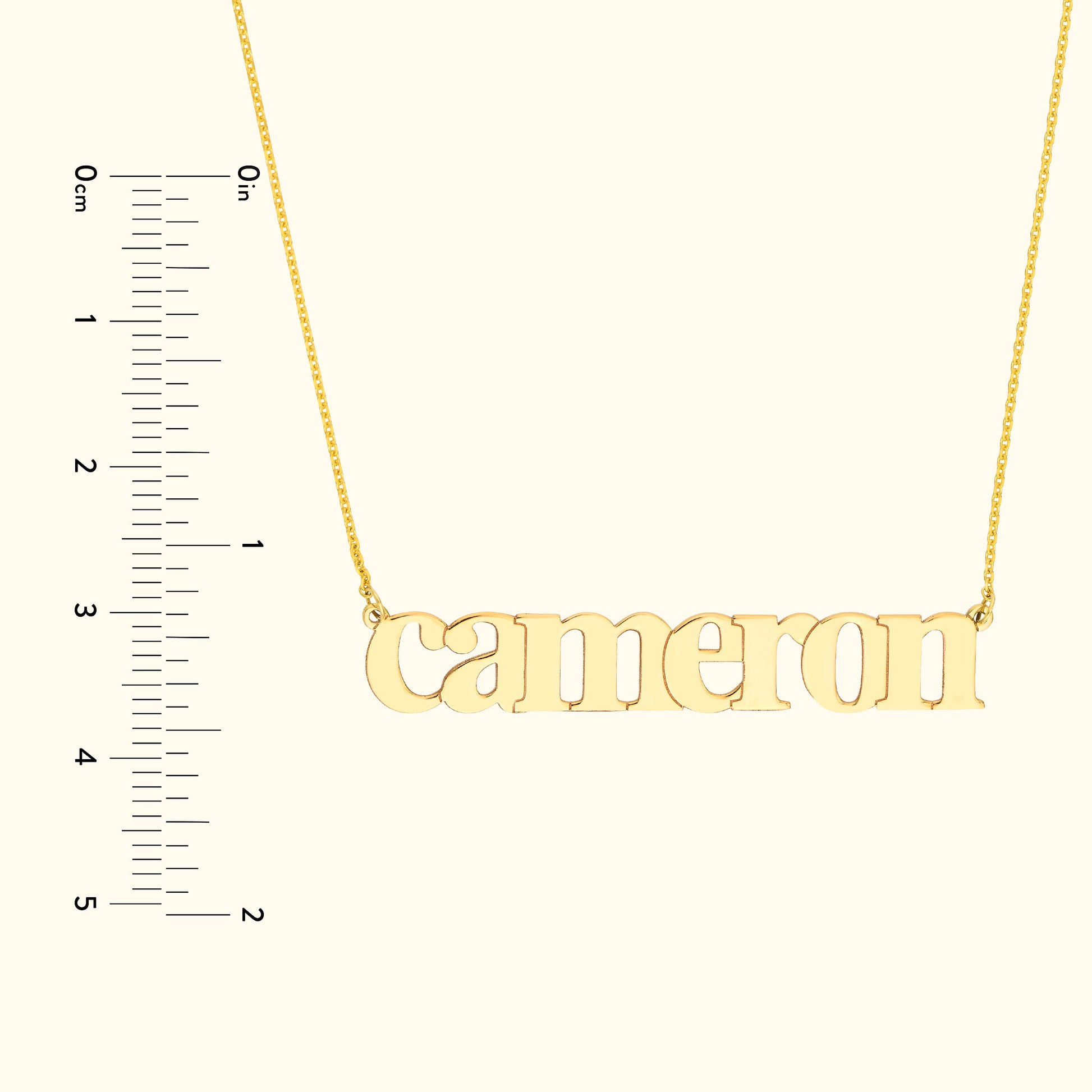 Gold name necklace spelling "cameron" on a simple chain with a ruler for size reference.
