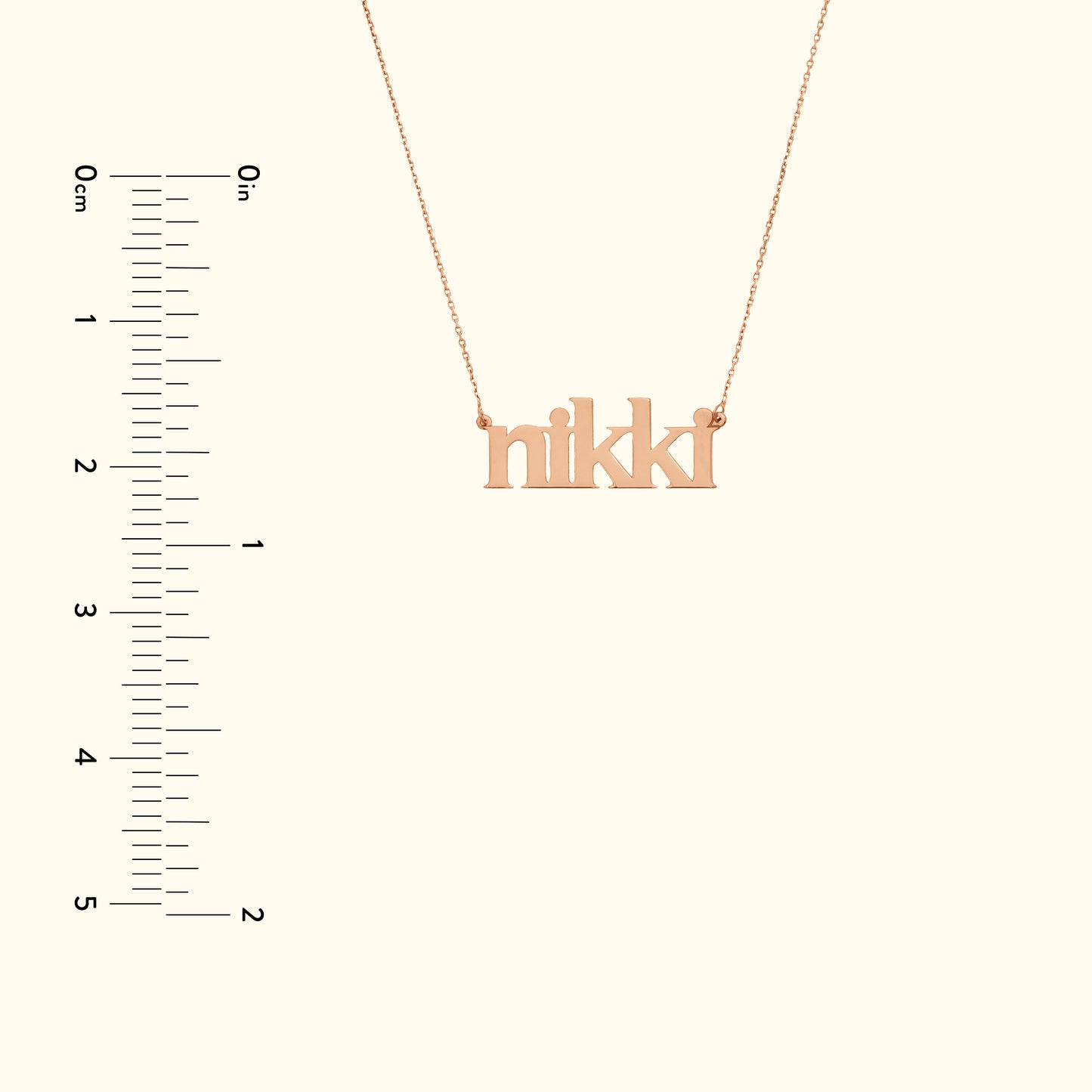 Rose gold name necklace spelling "nikki," displayed next to a measurement scale.