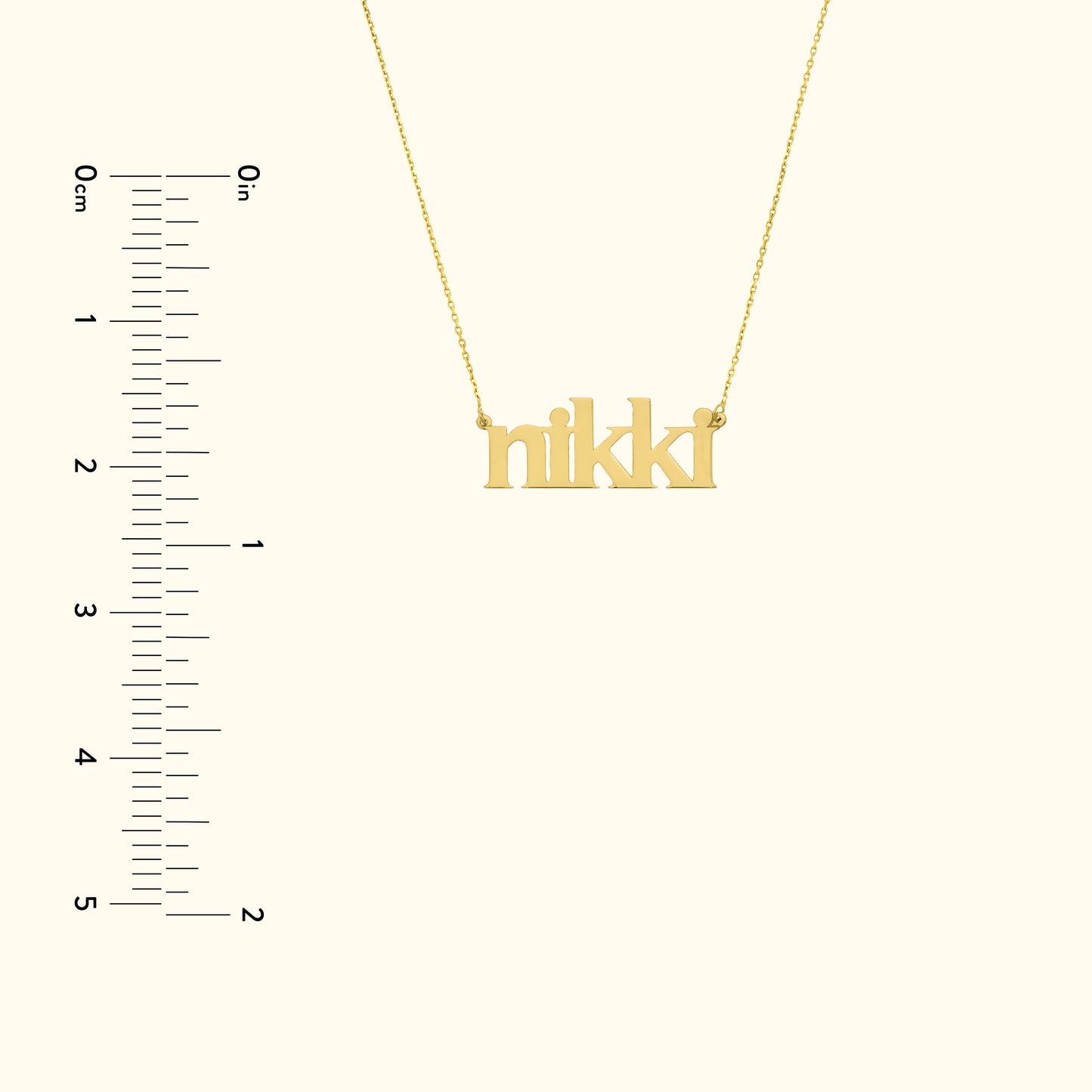 Gold necklace featuring the name "nikki" in a playful font, next to a ruler for scale.
