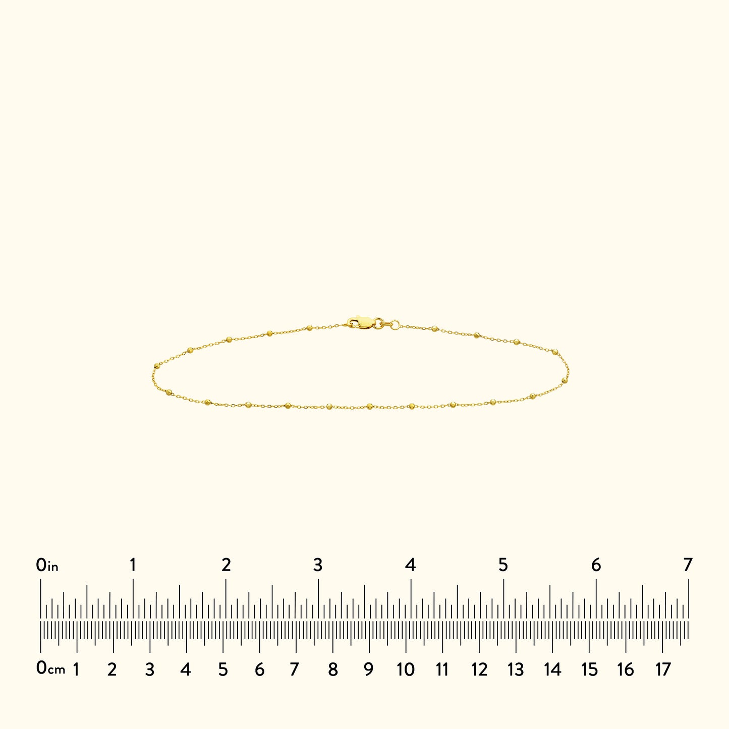 Thin gold bracelet with small decorative beads, displayed against a light background.
