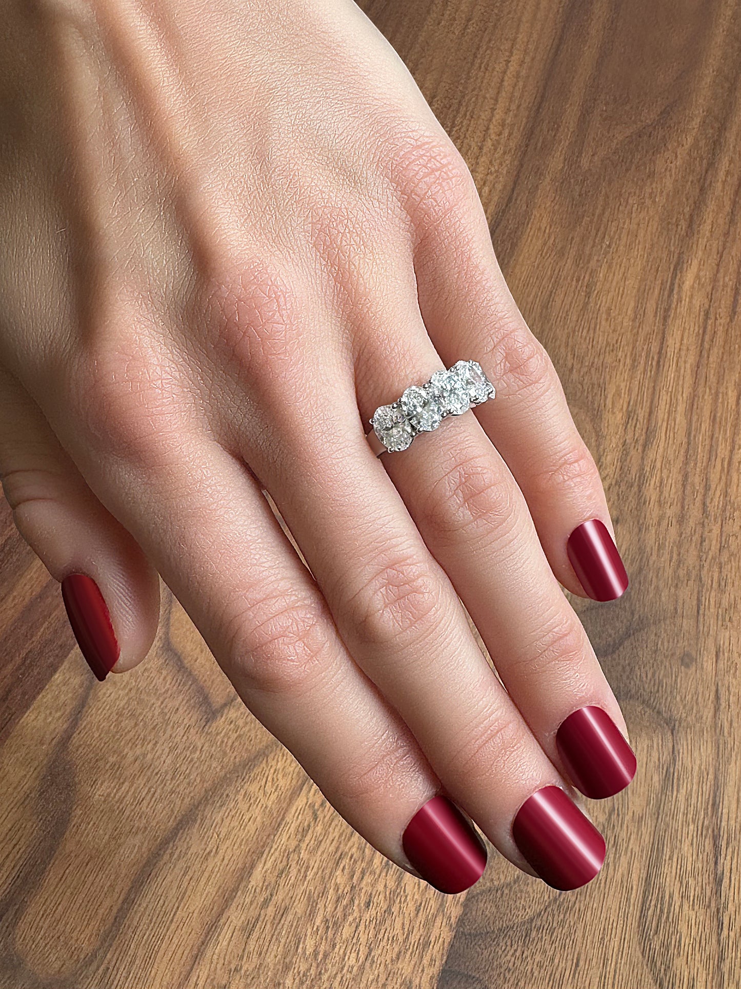 A hand with elegant red nails displays a diamond-studded silver ring on a wooden surface.