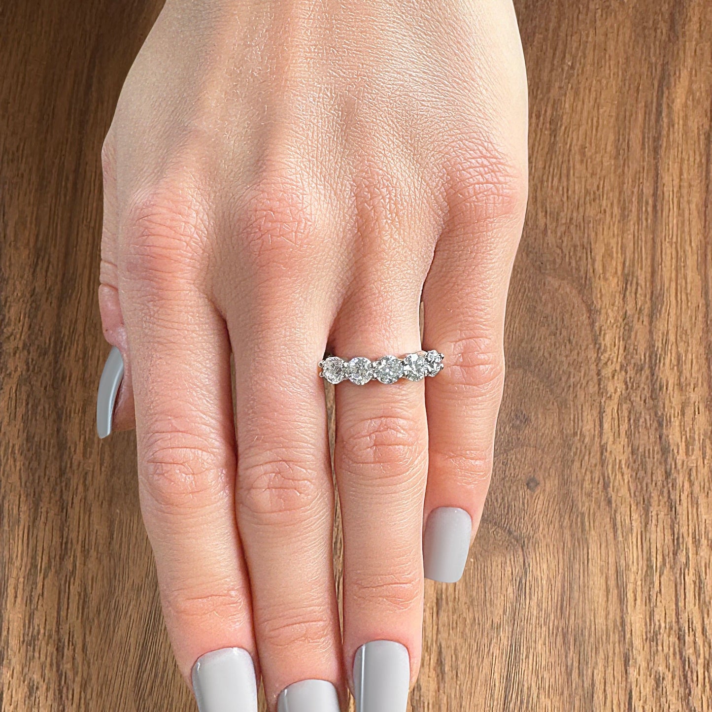 A hand with a silver diamond band ring, resting on a wooden surface.