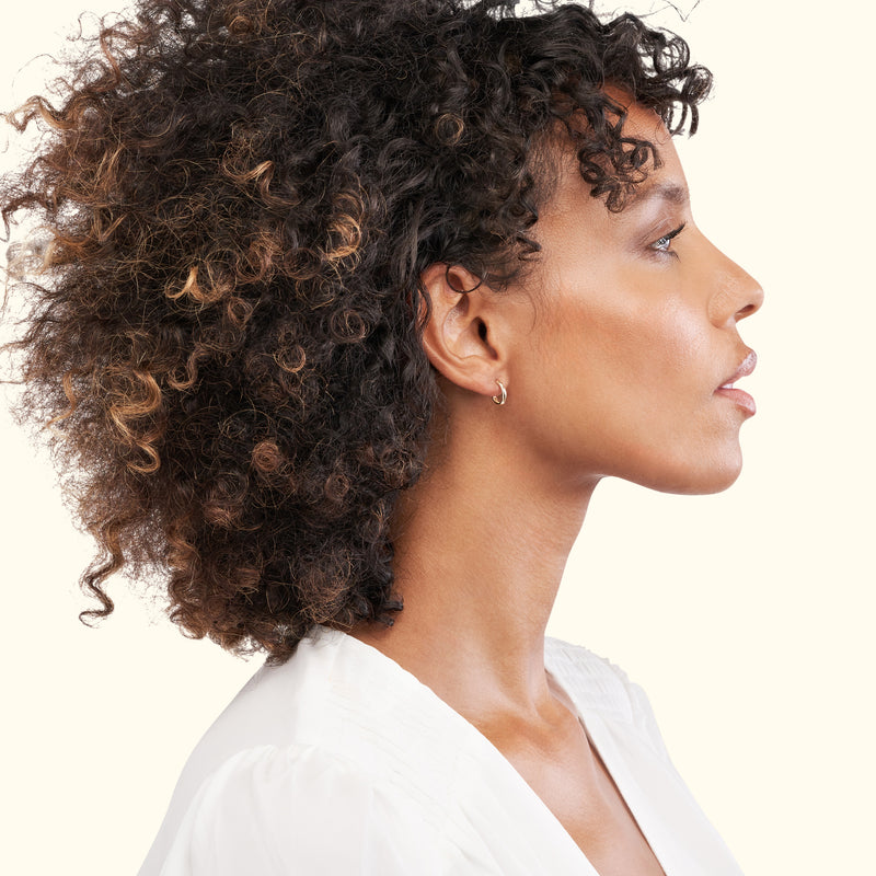 Profile view of a woman with curly hair wearing a small hoop earring.