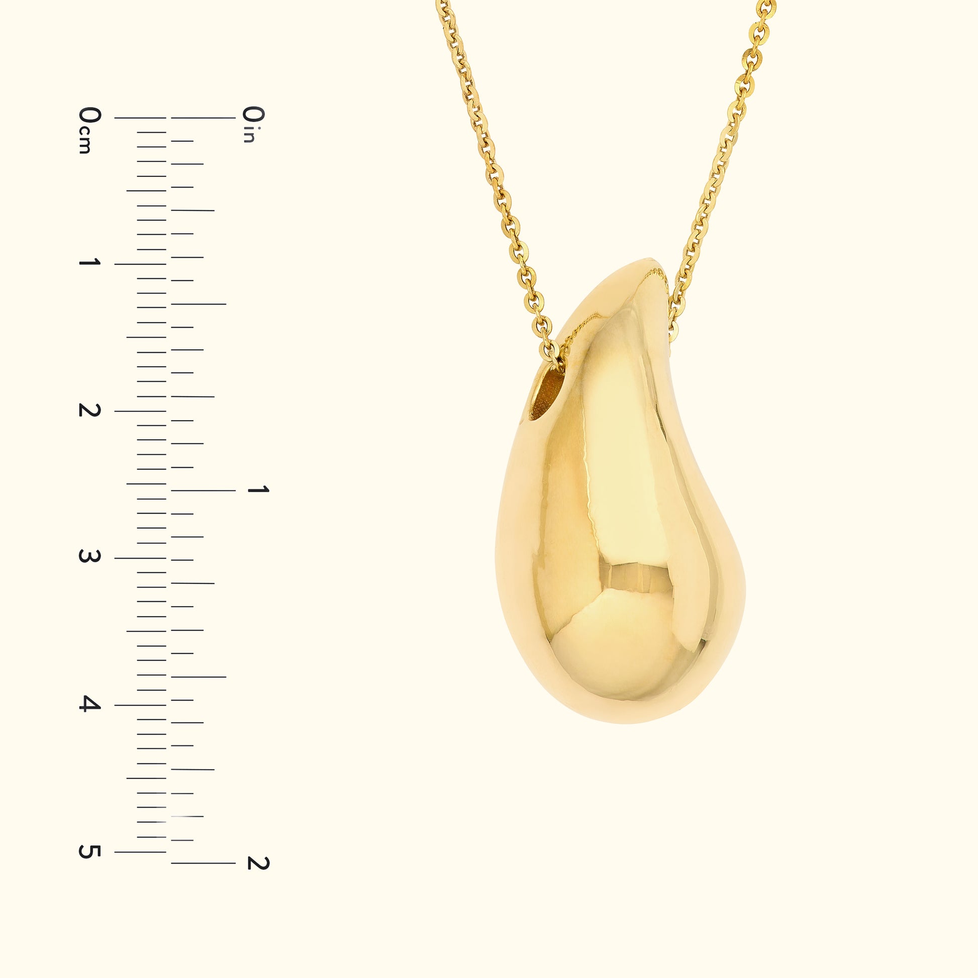 Smooth golden teardrop pendant hanging from a delicate chain, with a ruler for scale.