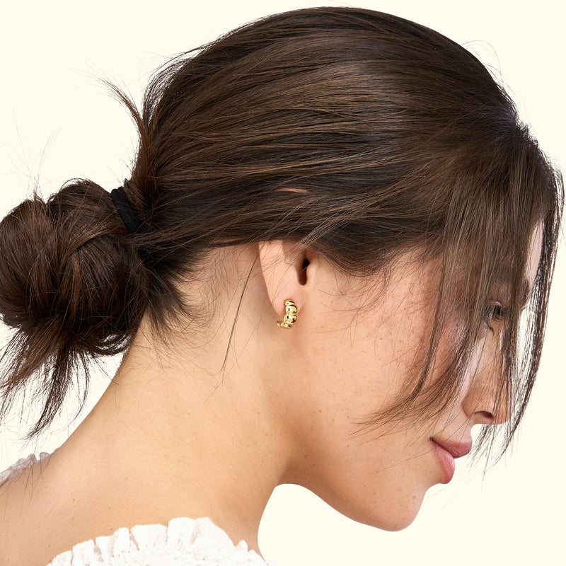 A woman in profile wears a gold earring, showcasing her elegant hairstyle and features.