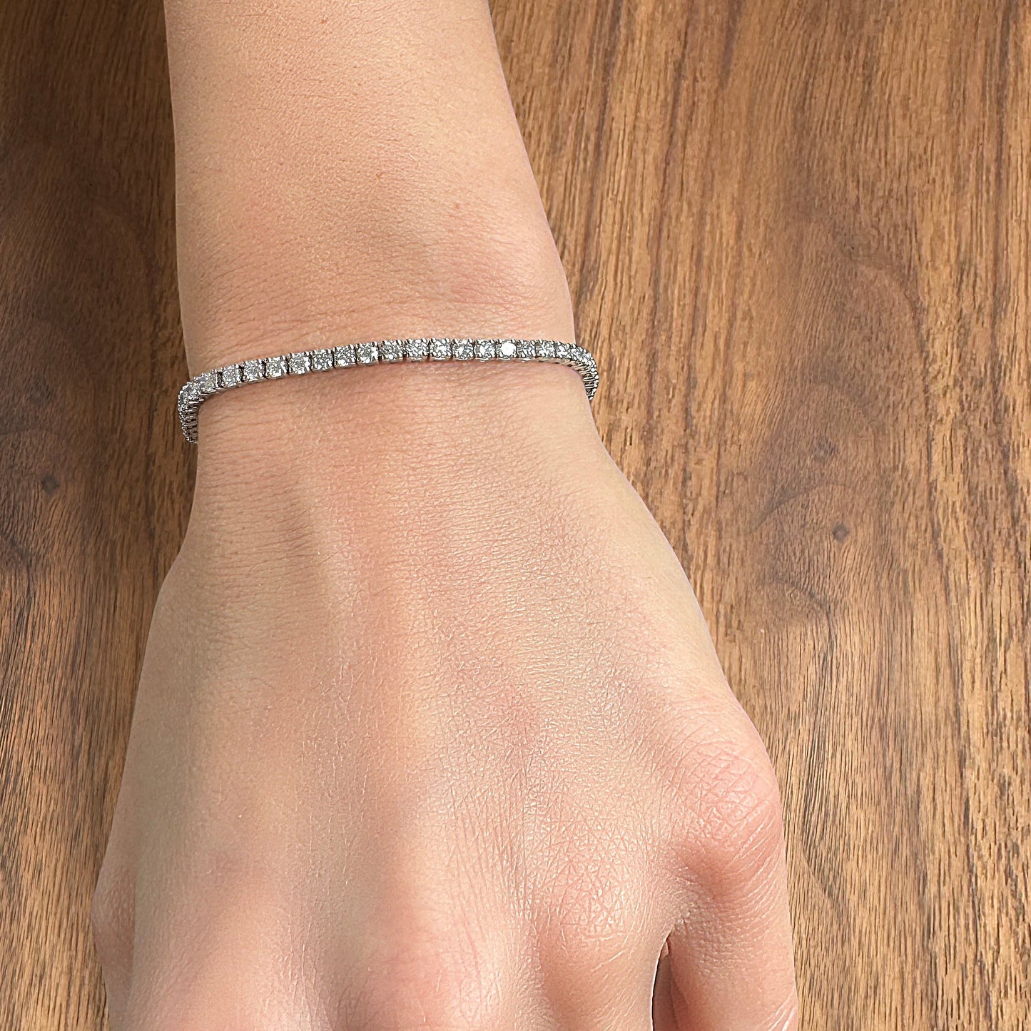 A sparkling diamond bracelet worn on a wrist against a wooden background.