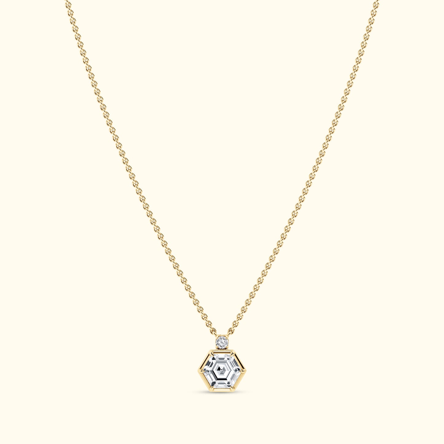 Gold necklace with a hexagonal diamond pendant on a light background.