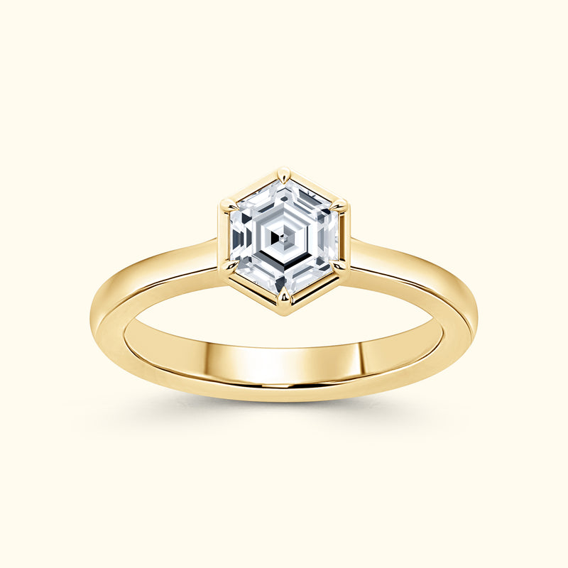 Gold ring with a hexagonal diamond centerpiece on a light background.